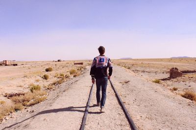 Full length of man walking on railroad tracks in desert