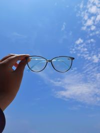 Human hand holding eyeglasses against sky