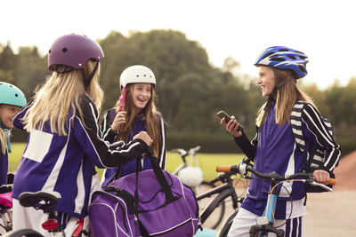 Happy girls wearing helmet standing with bicycles against sky
