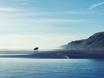 Person riding horse at beach against sky
