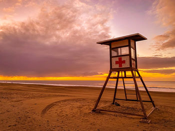 Lifeguard hut on beach against sky during sunset