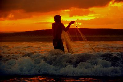 Rear view of man fishing in sea during sunset