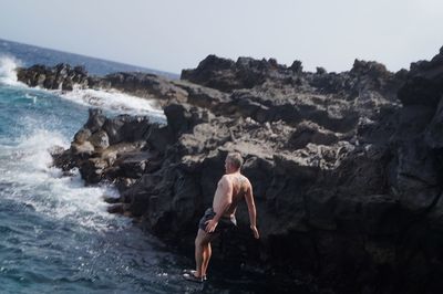 Rear view of woman standing on rocks at beach