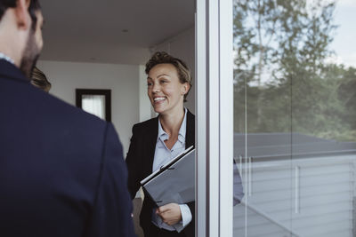 Smiling female real estate agent greeting couple entering in new house