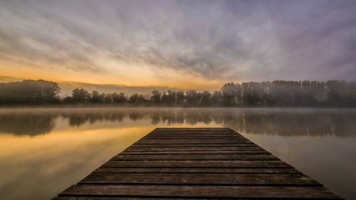 Pier over lake against sky during sunset