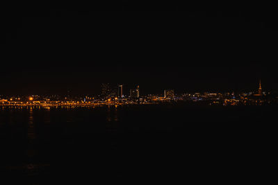 Illuminated city by sea against sky at night