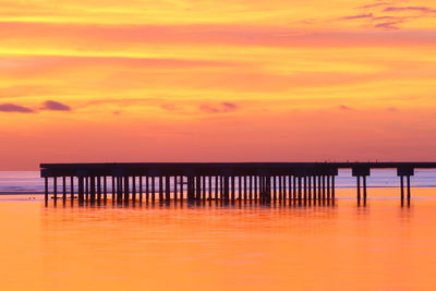 Silhouette pier on sea against orange sky