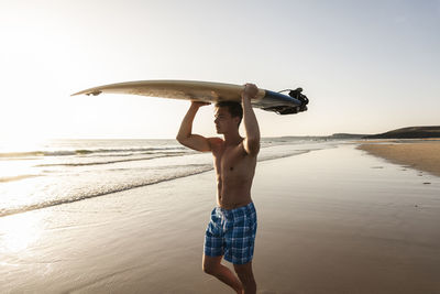 Young man walking on the beach, carrying his surfboard