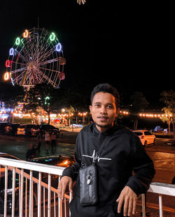 Portrait of young man standing at amusement park at night