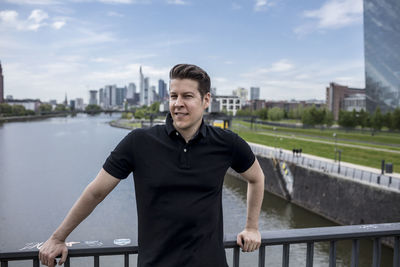 Portrait of smiling man standing on bridge over river