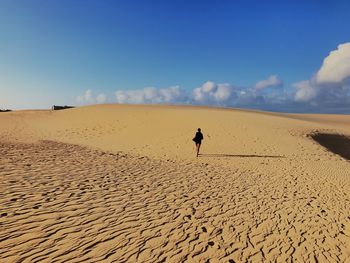 Man on sand dune in desert against blue sky
