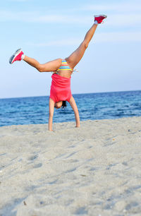 Woman doing a cartwheel on beach against sky