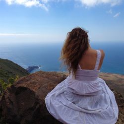 Rear view of woman looking at sea while sitting on rock