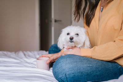 Midsection of woman with dog sitting on bed at home