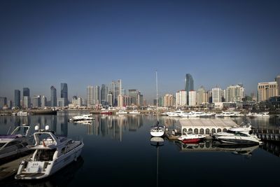 Boats in sea by cityscape against clear sky