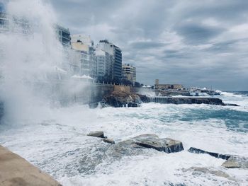 Sea waves splashing on shore against sky