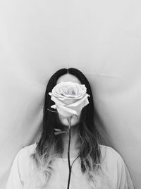 Woman with face covered by rose against curtain