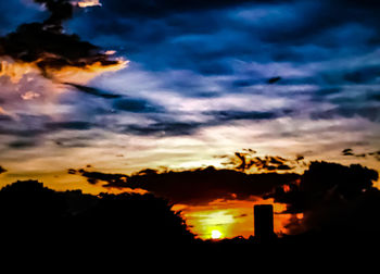 Silhouette trees against dramatic sky during sunset