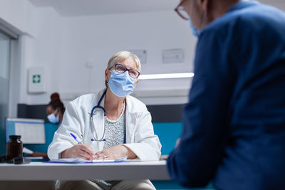 Female doctor wearing mask consulting patient in clinic