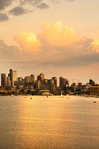 Buildings by sea against sky during sunset