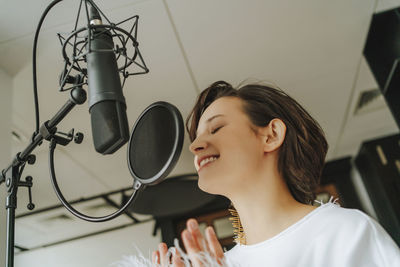 Smiling singer recording music through microphone in studio