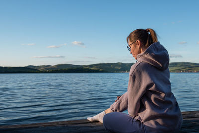 Woman sitting by lake against sky