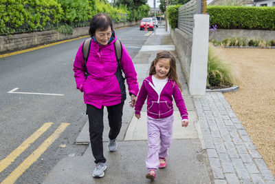 Full length of grandmother and granddaughter walking at sidewalk in city