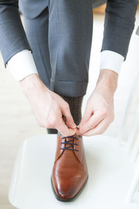 Low section of bridegroom tying shoelace on chair