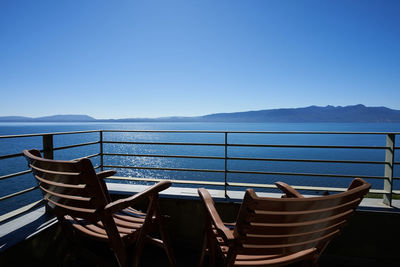 Empty chairs by sea against clear blue sky