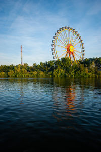 Ferris wheel by lake against sky