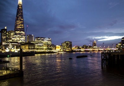 River by illuminated buildings against sky at dusk