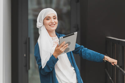 Young woman in hijab using digital tablet standing outdoors