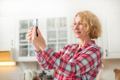 Mature woman taking selfie from mobile phone in kitchen at home