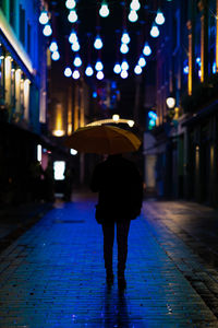 Rear view of woman walking on wet street at night