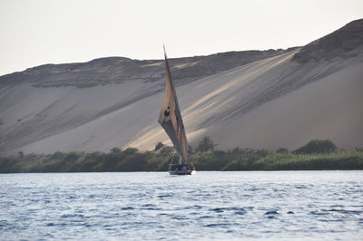Sailboat sailing on sea against mountain