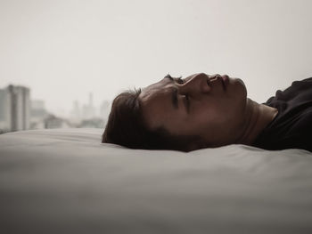 Asian man feels sad alone on bed with city background. stay home, depression and loneliness concept.