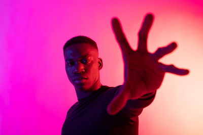 Portrait of young man standing against pink background