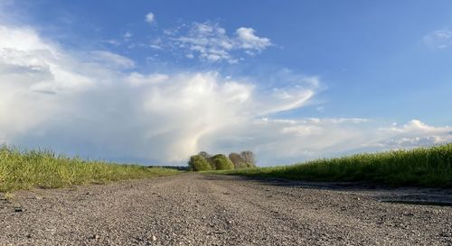 Dirt road amidst field against sky