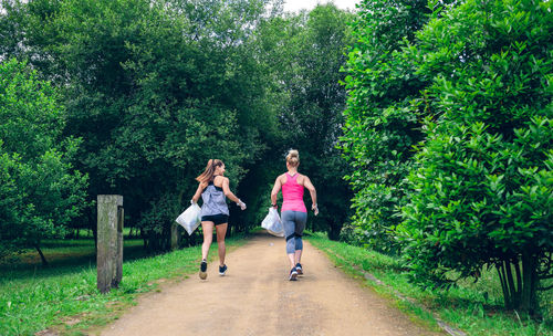 Rear view of female friends running on footpath at park