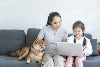 Smiling mother and daughter using laptop while sitting with dog on sofa