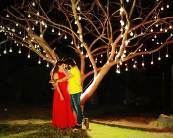 Woman standing by illuminated tree at night