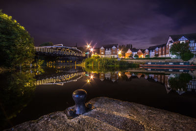 Bridge and houses reflection in lake against sky at night