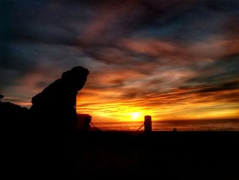 Silhouette beach against dramatic sky during sunset