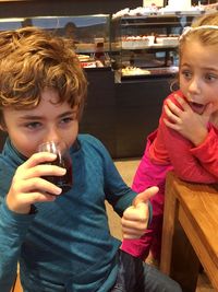 Shocked girl looking at boy drinking from glass at restaurant