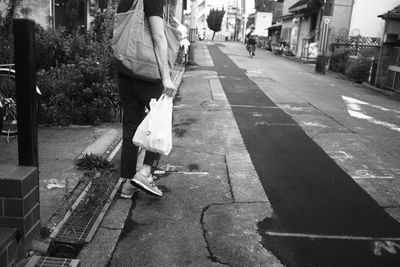 Low section of woman holding shopping bag on street amidst buildings