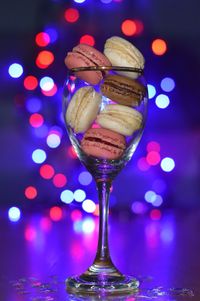 Close-up of macaroons in wineglass on table against illuminated christmas tree