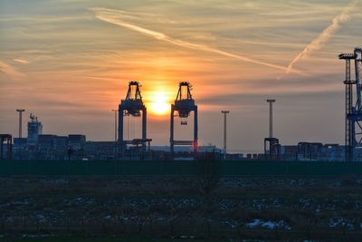 Factory by buildings against sky during sunset