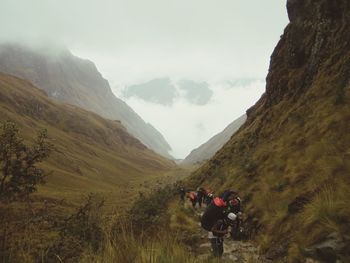 Hikers walking on mountain against sky during foggy weather