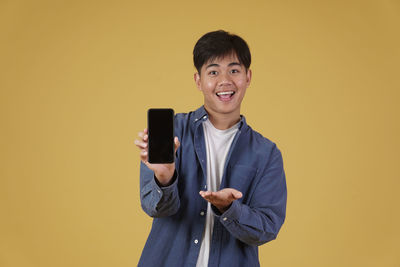 Portrait of smiling young man standing against yellow background