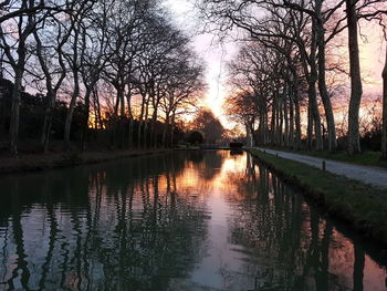 Silhouette bare trees by lake against sky during sunset